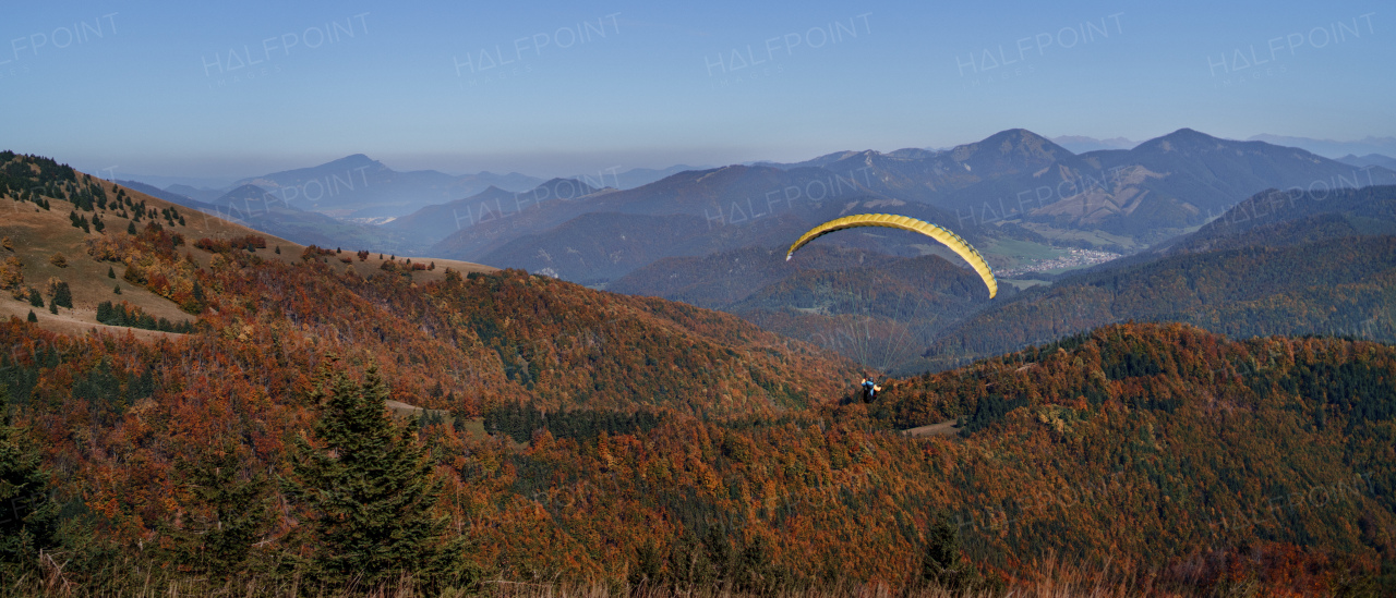 A paraglider flying in the blue sky with mountain in background.