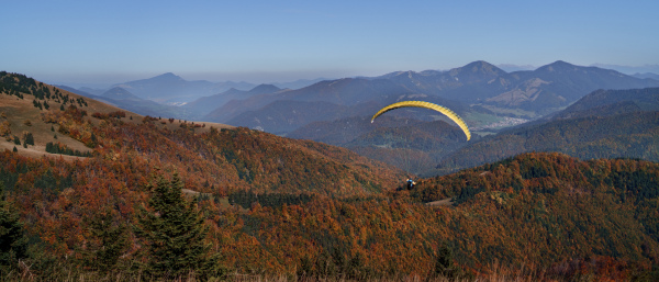 A paraglider flying in the blue sky with mountain in background.