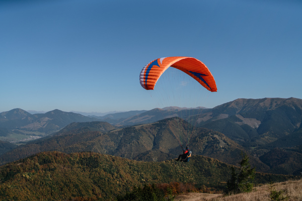 A paraglider flying in the blue sky with mountain in background.