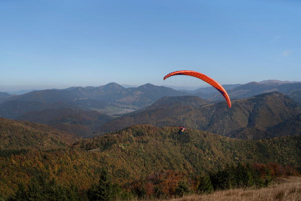 A paraglider flying in the blue sky with mountain in background.