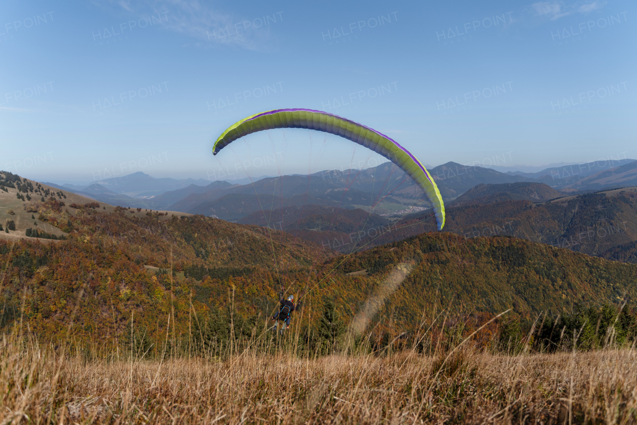 A paraglider flying in the blue sky with mountain in background.