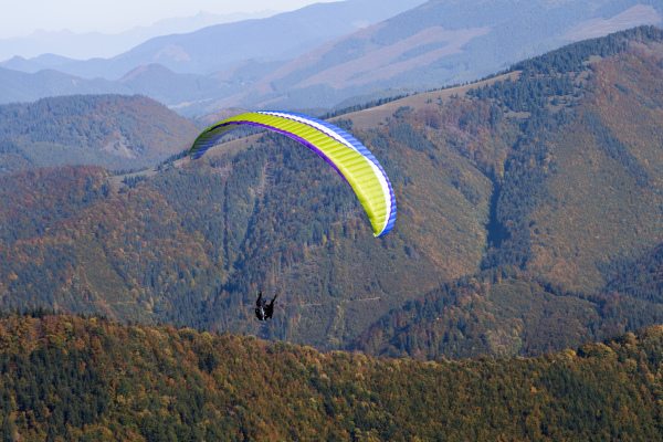 Paragliders flying in a blue sky with mountain in background.