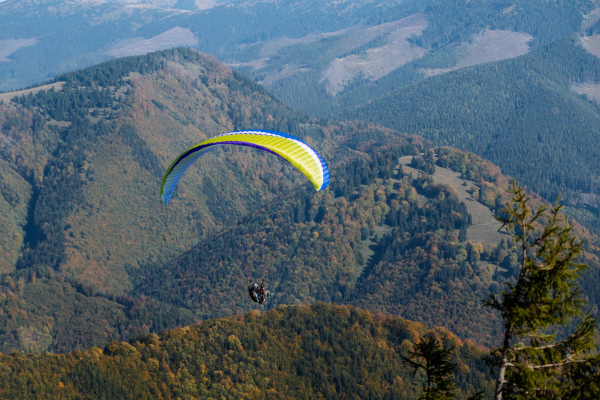 A paraglider flying in the blue sky with mountain in background.