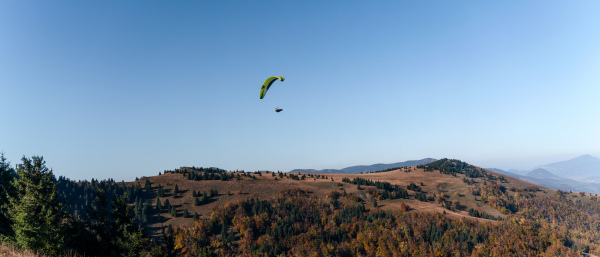 A paraglider flying in the blue sky with mountain in background.