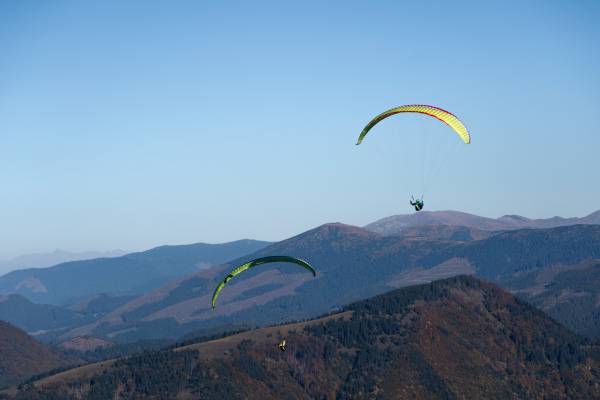 Paragliders flying in a blue sky with mountain in background.