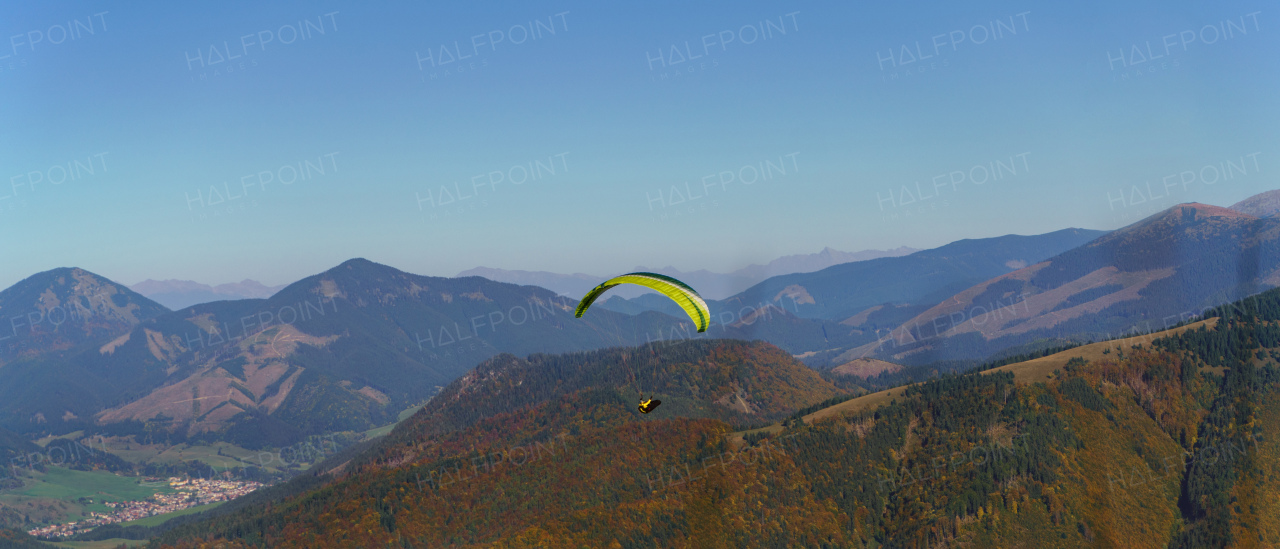 A paraglider flying in the blue sky with mountain in background.