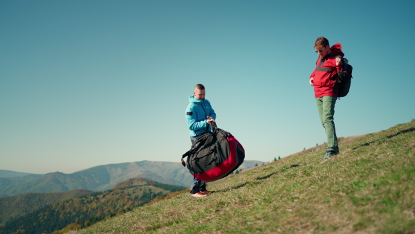 Paragliders walking up hill to paragliding starting point, on a sunny morning in mountains.