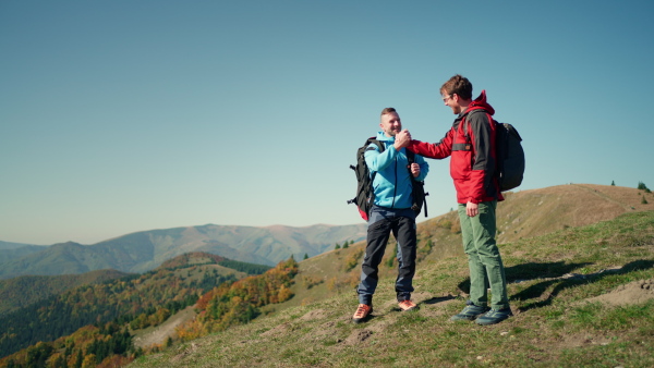 Paragliders high fiving after walking up hill to a paragliding starting point, on a sunny morning in mountains.