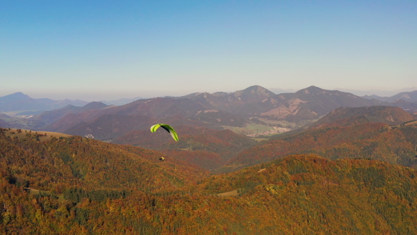 A paraglider flying in the blue sky with mountain in background.