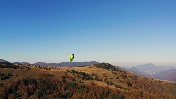 A paraglider flying in the blue sky with mountain in background.