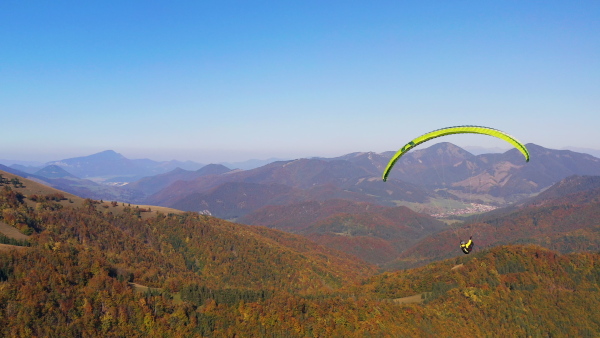 A paraglider flying in the blue sky with mountain in background.