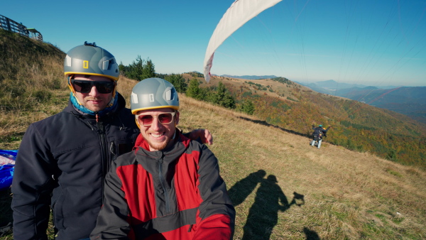 A portrait of two paragliders preparing for the flight on mountain, looking at camera. Extreme sports activity.