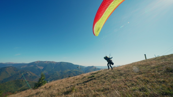 A paraglider taking off in the blue sky with mountain in background.