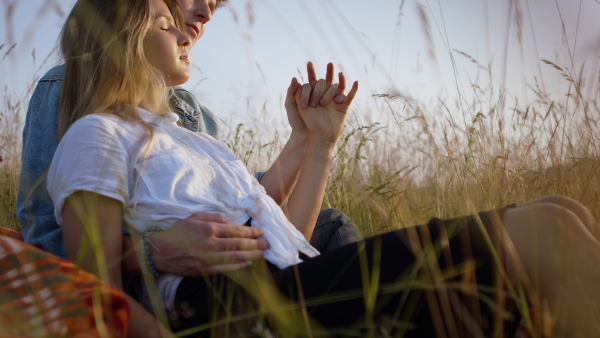 Beautiful young couple outside sitting on meadow, holding hands and having a romantic time.