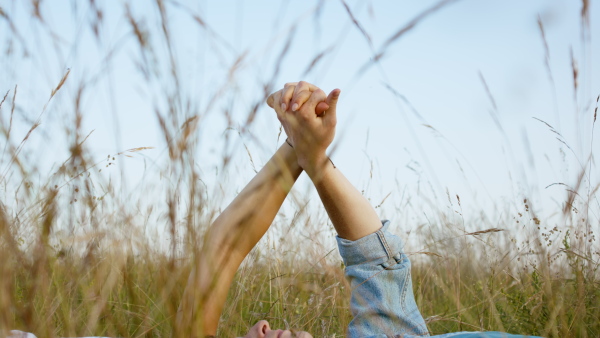 Beautiful young couple outside laying on meadow, holding hands and having a romantic time.