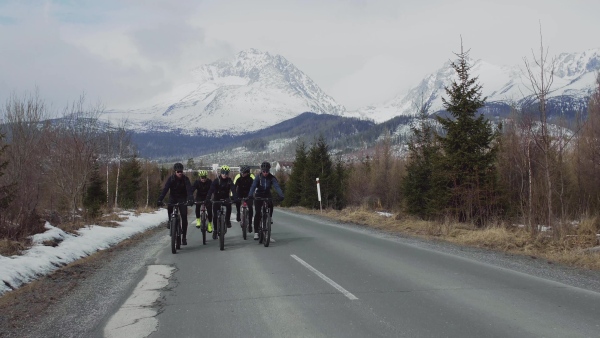 A group of mountain bikers riding on road outdoors in winter, mountains in the background.