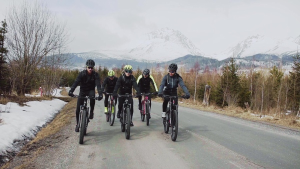 A group of mountain bikers riding on road outdoors in winter, mountains in the background. Slow motion.