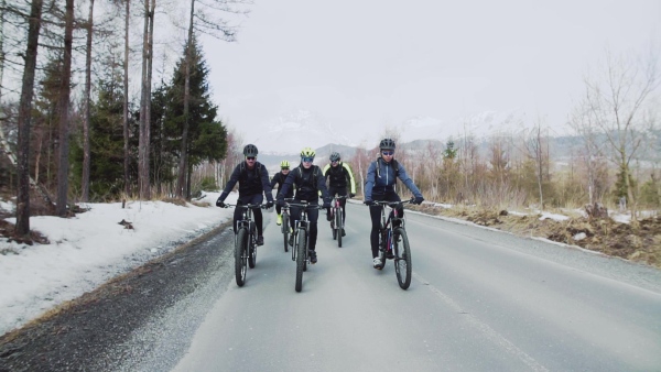 A group of mountain bikers riding on road outdoors in winter, mountains in the background. Slow motion.