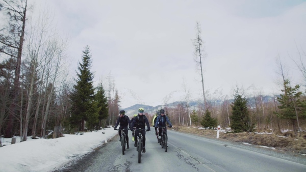 A group of mountain bikers riding on road outdoors in winter, mountains in the background. Slow motion.