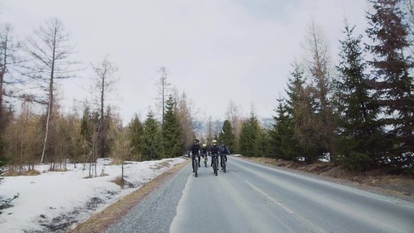 A group of mountain bikers riding on road outdoors in winter, mountains in the background. Slow motion.