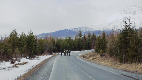 A group of mountain bikers riding on road outdoors in winter, mountains in the background. Slow motion.