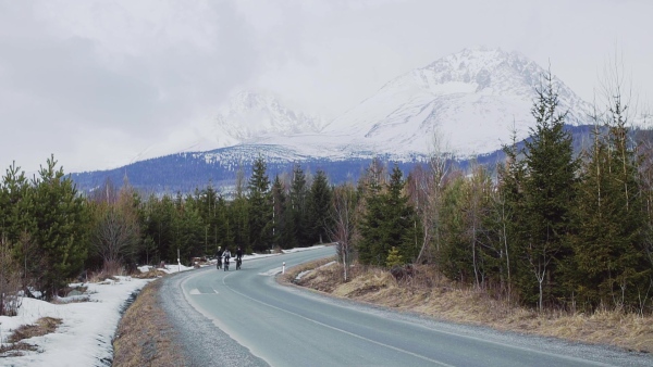 A group of mountain bikers riding on road outdoors in winter, mountains in the background. Slow motion.