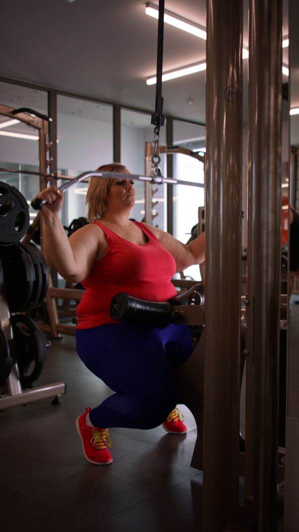 A vertical footage of fat woman working out on a lat pulldown machine indoors in gym