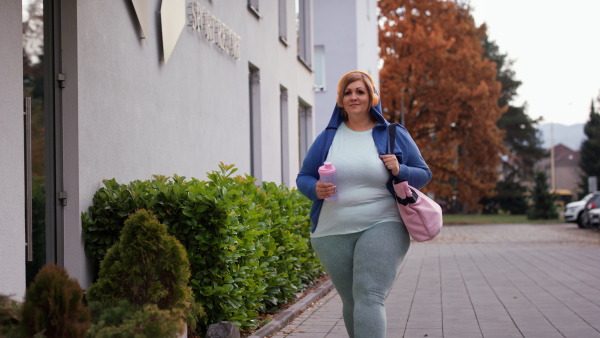 A happy overweight woman in sports clothes outdoors on the way to fitness center