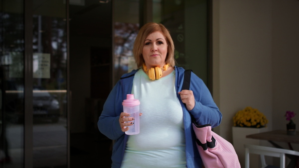 A happy overweight woman in sports clothes outdoors on the way to fitness center