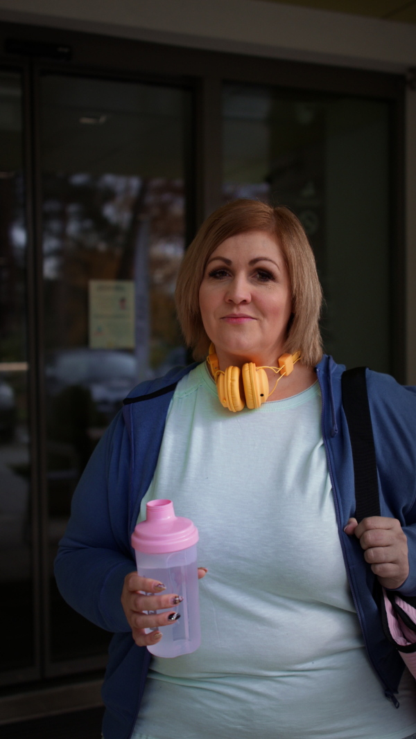 A happy overweight woman in sports clothes outdoors on the way to fitness center