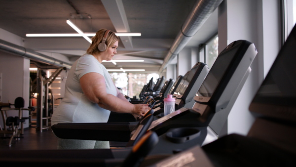 An overweight woman with headphones exercising on treadmill in gym