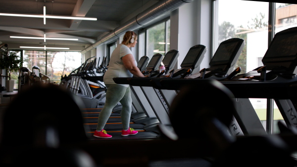 An overweight woman with headphones exercising on treadmill in gym