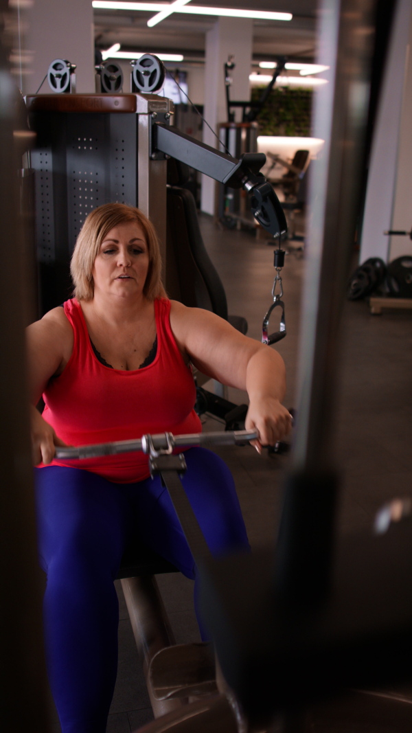 A vertical footage of fat woman working out on a lat pulldown machine indoors in gym