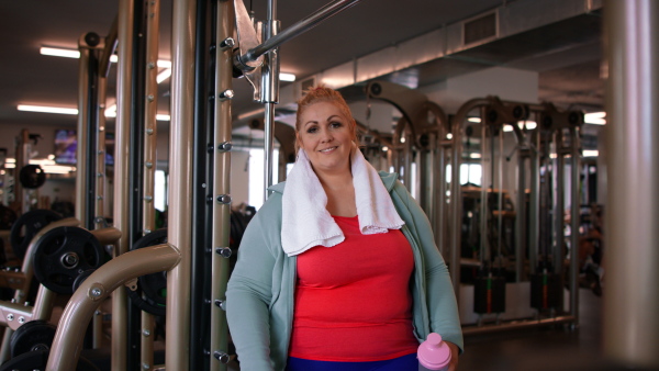 A happy fat woman after exercise indoors in gym, looking at camera.