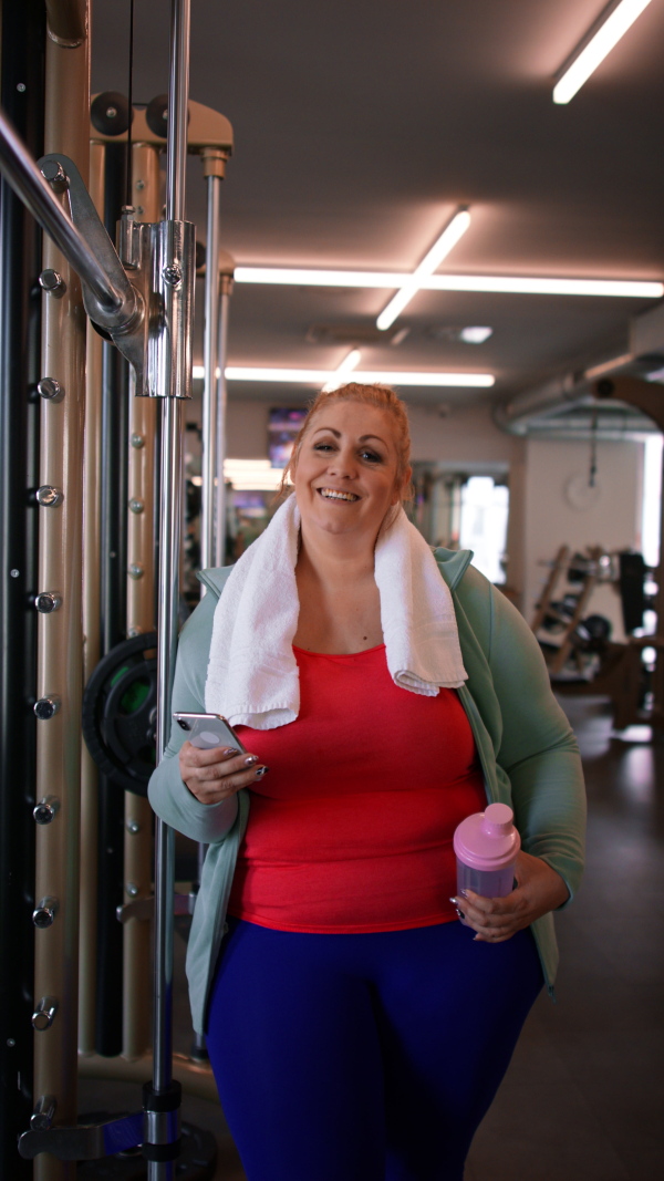 A happy fat woman after exercise indoors in gym, looking at camera.