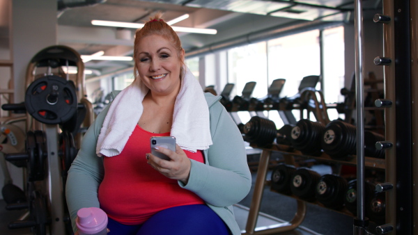 A happy fat woman after exercise indoors in gym, looking at camera.