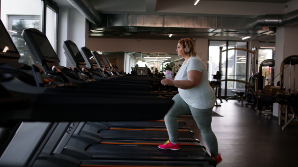 An overweight woman with headphones exercising on treadmill in gym