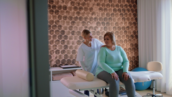 A physiotherapist woman exercising with overweight woman indoors in rehabilitation center