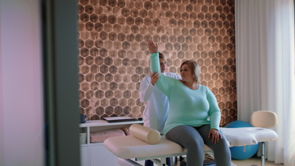 A physiotherapist woman exercising with overweight woman indoors in rehabilitation center