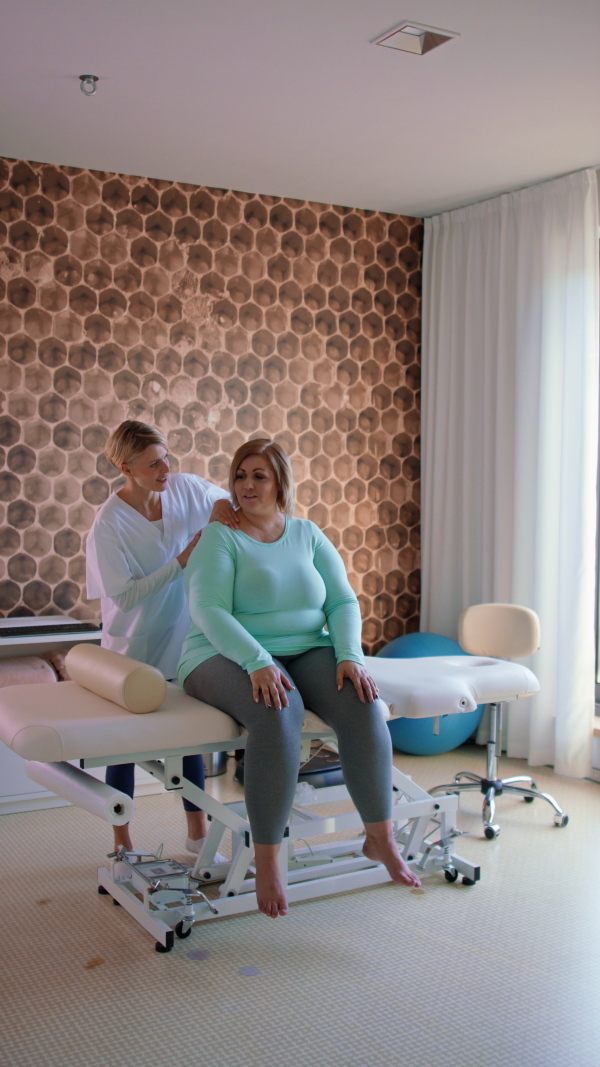 A vertical footage physiotherapist woman exercising with overweight woman indoors in rehabilitation center