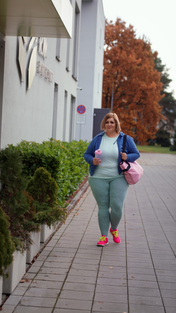 A vertical footage of happy overweight woman in sports clothes outdoors on the way to fitness center