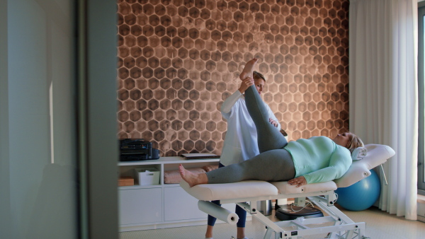 A physiotherapist woman exercising with overweight woman indoors in rehabilitation center