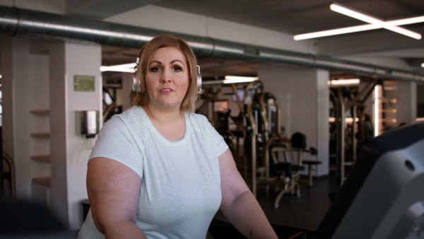 Mid adult overweight woman with headphones running on treadmill in gym