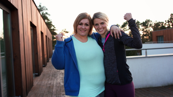 A happy overweight woman high fiving with personal trainer outdoors on gym terrace.