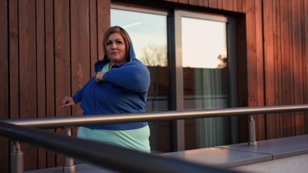 A mid adult plus size woman stretching after work out training outdoors on terrace of gym