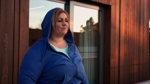 A mid adult plus size woman stretching after work out training outdoors on terrace of gym