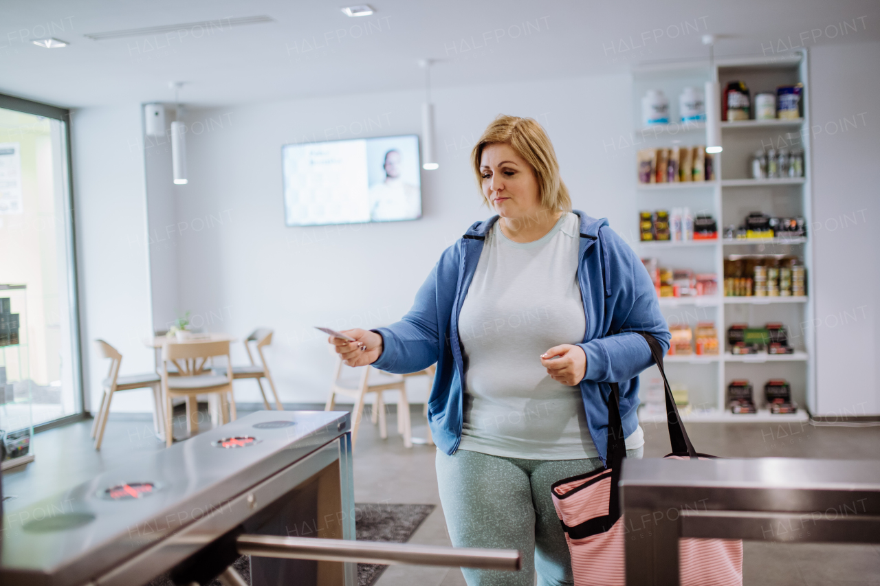 An overweight woman using smartphone to open automatic gate machine in gym