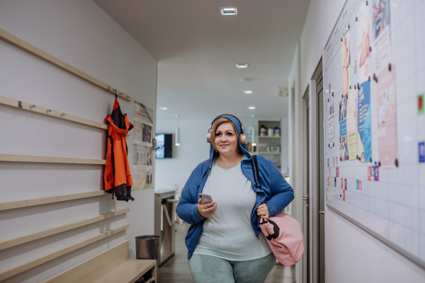 A happy overweight woman in sports clothes indoors in corridor on the way to gym