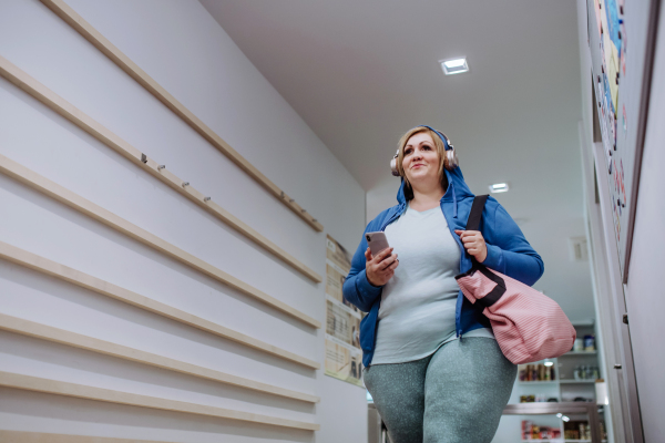 A low angle view of happy overweight woman in sports clothes indoors in corridor on the way to gym