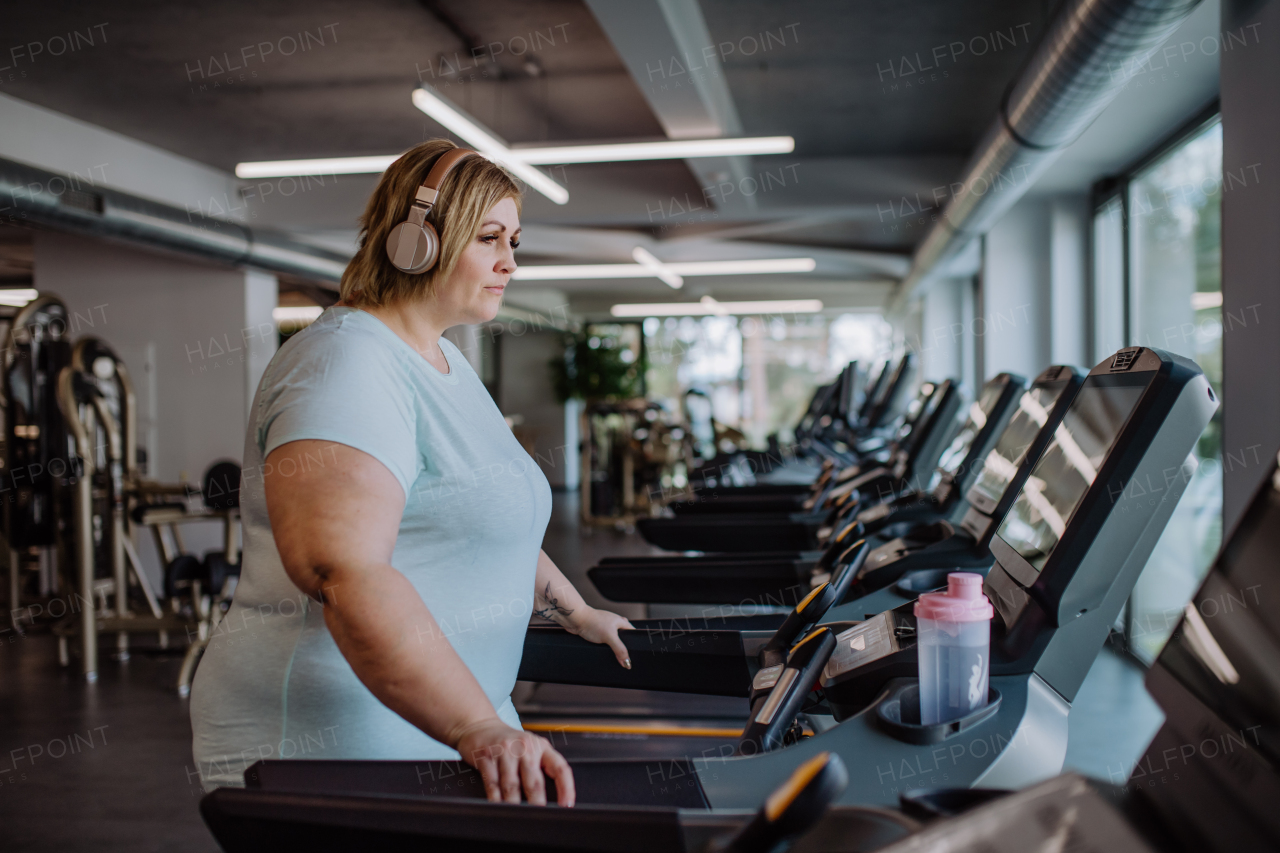 Mid adult overweight woman with headphones running on treadmill in gym